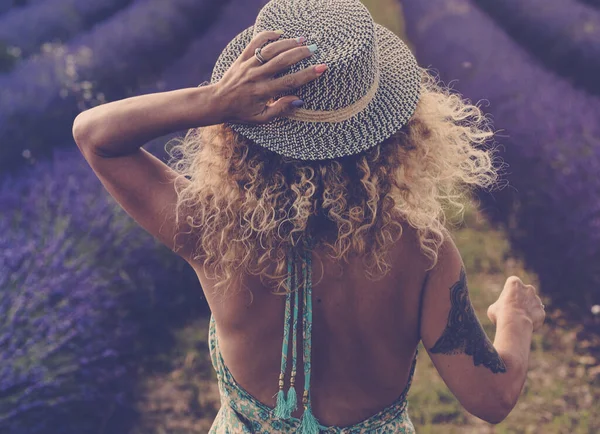 在户外自然探险生活中 穿着布荷花漂亮衣服 戴着旅行风格的帽子 头戴金色卷曲的漂亮长发 走在薰衣草地里的美女的背影 或者是免费的女人 — 图库照片