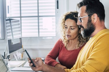 Smart working at home free office lifestyle with adult couple using home and two pc laptop computer on the desktop - modern man and woman online job remote workers bright day light