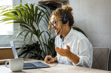 Gözlüklü kıvırcık kadın dizüstü bilgisayar kullanıyor, evdeki müşteriyle internet üzerinden iletişim kuruyor, rahat çalışma odası, uzaktan çalışma, e-öğrenme konsepti