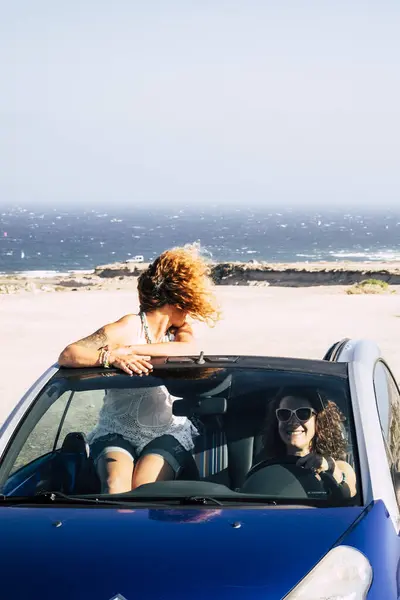 Car travel friends transportation two happy women enjoy convertible auto together in summer trip holiday vacation - ocean and beach in background - driving and having fun concept