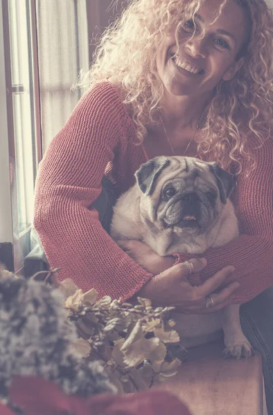 Dog and woman best friends concept and happiness - young beautiful cheerful woman hug and enjoy her pug pet at home - friendship human and animals lifestyle for joyful emotions
