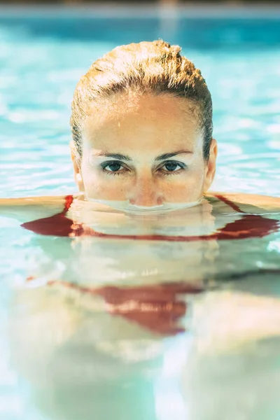 Portrait of woman with face down the water at the pool and eyes outside looking at the camera - adult pretty woman people enjoy water and healthy lifestyle swimming in summer