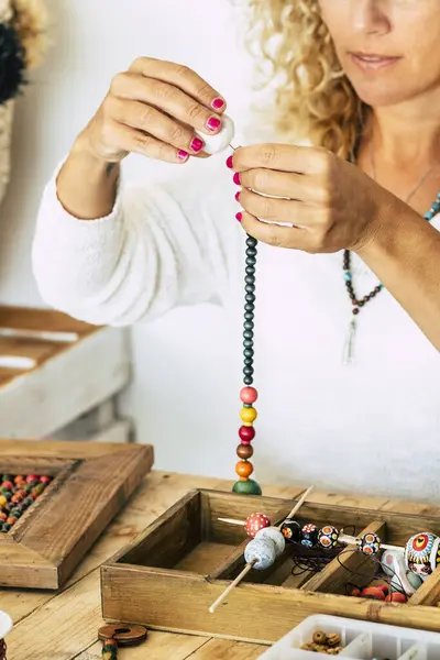 Woman at home make handmade jewelry. Box with beads on old wooden table. view with woman hands - tutorial to learn how to make bracelets and jewelry online and alternative home job