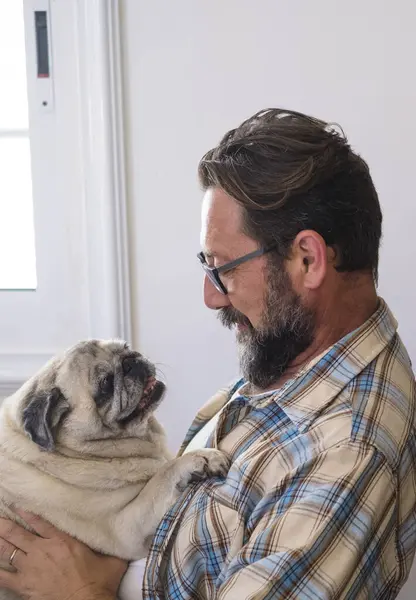 Happy adult  man hug and play with his old best friend dog pug at home - people and lovely animal life indoor