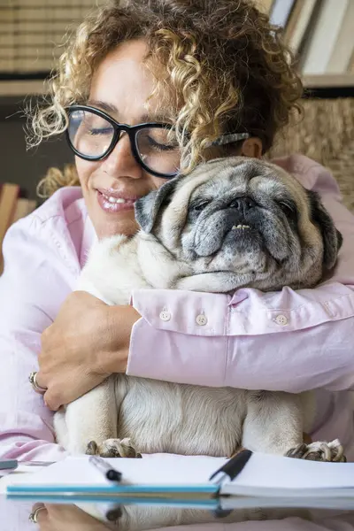 People dog owner and happy lifestyle at home together - woman hug her pug and work on computer in room office indoor - affection and best friend concept