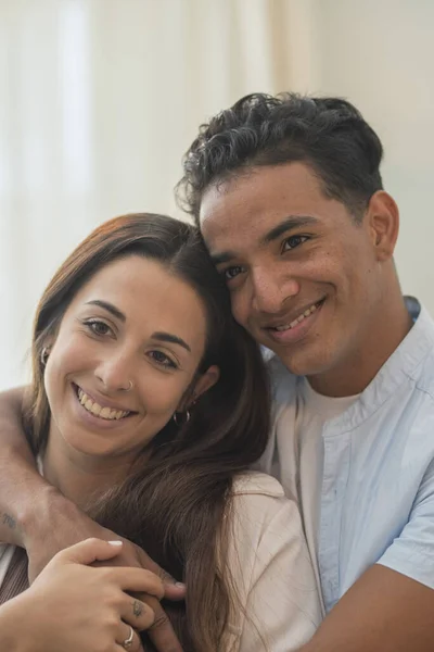 Young millennial interracial couple hug with love at home in living room - relationship with black boy and caucasian girl together standing and embracing looking each other - concept of life and house