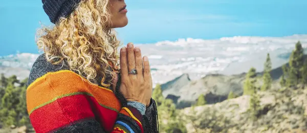 Close-up of calm young Caucasian woman holding hands on heart chest and feeling grateful and grateful. Happy female shows gratitude, love and care, prays or displays. Religion, faith concept.