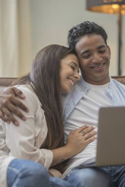 Genç çift yeni bir ev bilgisayar laptop kullanarak kanepede oturan rahatlatıcı, yeni daireye taşımak için mutlu gülümseyen hareket