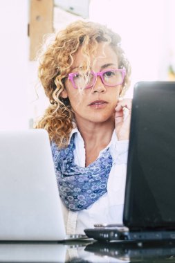 İki dizüstü bilgisayarı olan Kafkasyalı kadın ofis çalışanı - iş kadını ve akıllı iş hayatı çalışanları - yetişkin görünümü bilgisayar ekranı ve İnternet eğitimi