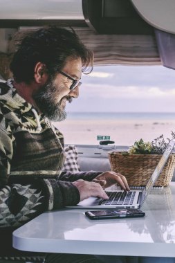 Adult man use laptop computer to work inside camper van with roaming phone connection. Concept of modern people lifestyle in smart working or travel digital nomad freedom