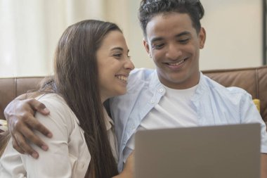 Genç çift yeni bir ev bilgisayar laptop kullanarak kanepede oturan rahatlatıcı, yeni daireye taşımak için mutlu gülümseyen hareket
