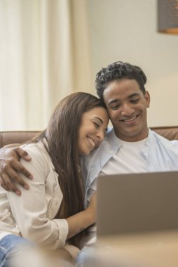 Genç çift yeni bir ev bilgisayar laptop kullanarak kanepede oturan rahatlatıcı, yeni daireye taşımak için mutlu gülümseyen hareket