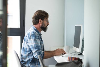 Kafkasyalı serbest çalışan bir adam masanın başında oturmuş internete bağlı internet işi için yazı yazıyor. Evde çalışan hippi yetişkin bir erkek. 