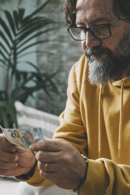 Ekonomi ve para sorunu olan insanlar. Yüzünde endişeli bir ifadeyle elinde nakit para tutan bir adam. Son 20 avroyu koltukta oturan olgun, beyaz bir adam. Gerçek hayatta nakit ve fatura ödemeleri