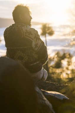 İnsanlar ve doğa yaşam tarzı kavramı - kayaların üzerinde oturan ve arka planda güzel günbatımının ve manzaranın tadını çıkaran adam - dağ turizmi tatil yaşam tarzı