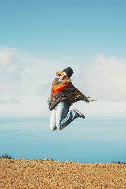 Turist hayatı yaşayan insanları gezmek. Neşeli, mutlu bir kadın, neşeyle atlıyor harika bir okyanusa ve mavi gökyüzüne. Yetişkin kadınlar için dünya varış ve özgürlük