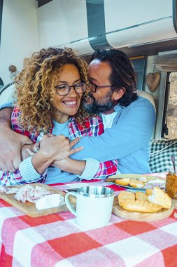 Öğle yemeği saatinde karavanın içinde birbirine sarılan neşeli bir çift. Seyahat ve tatil kavramı. Yetişkinler için karavan kiralamak. Hayat tarzını ve minibüs hayatını. Şebeke dışı