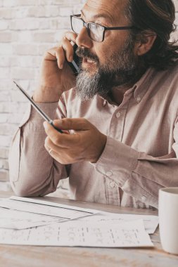 Masada oturan profesyonel bir işçi konuşuyor. İş adamı cep telefonuyla konuşuyor. Kağıtlar ve iş. Profesyonel insan sesle iletişim kurar. İş adamı etkinliği