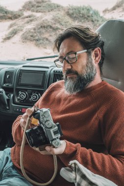 Karavanda oturan adam kamerayla çekilmiş fotoğrafları gözlemler. Erkek gezgin, tekerlekli evinde rahatlar.