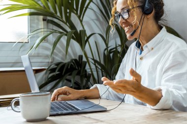 Gözlüklü kıvırcık kadın dizüstü bilgisayar kullanıyor, evdeki müşteriyle internet üzerinden iletişim kuruyor, rahat çalışma odası, uzaktan çalışma, e-öğrenme konsepti