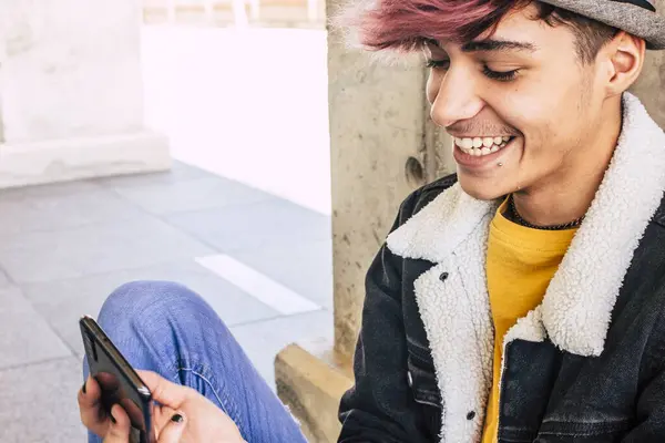 若い現代のティーンエイジャーは メッセージやソーシャルメディアの生活に電話アプリを使用して地面に座っています 都市生活の背景で流行のファッションの代替服とオンライン接続された青少年少年 — ストック写真