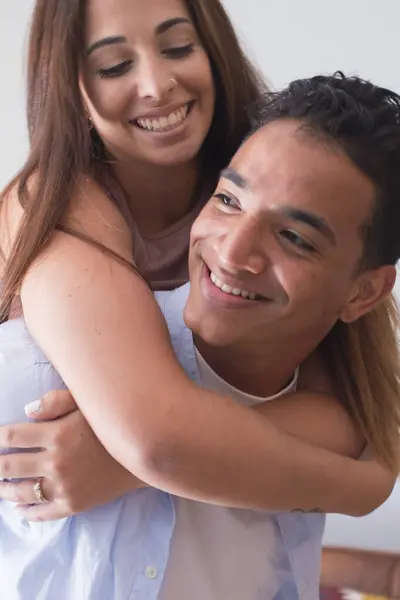 Smiling young man carrying woman on his back and laughing at home - young couple people in piggyback have fun together enjoying friendship and relationship indoor