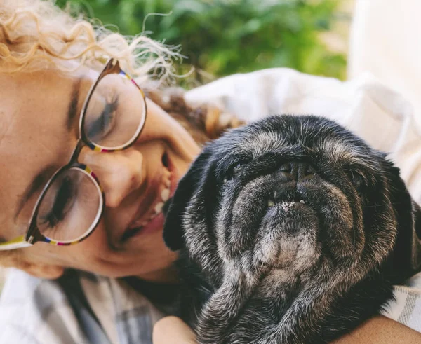 Cheerful woman hugging black old dog with love and friendship. Animal pug best friend forever. Female people and her puppy enjoying time together with happiness. Lady smiling and bonding dog