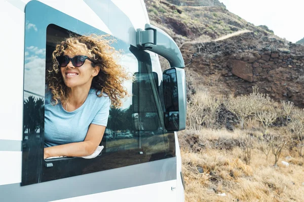 İnsanlar ve tatil beldeleri. Genç ve mutlu bir kadın gülümseyip modern karavan karavan minibüsünün penceresinin önünde doğanın tadını çıkarıyor. Dişi gezgin