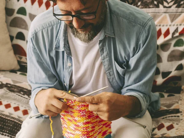 man at home busy in new hobby activity doing knitting work with wool and needles. Single male mature in indoor leisure activity alone. People in alternative work. Sitting on sofa in apartment