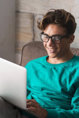 Evde internet ve dizüstü bilgisayarla çalışan beyaz bir öğrenci kanepede oturuyor - ev okulu konsepti - video konferansı ve insanlarla iletişim - mutlu çocuk