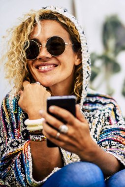 Güzel bir kadın cep telefonu kullanır ve gülümser. İnsanlar kış sezonunun tadını çıkarırlar. Güneş gözlüklü, ceketli ve mavi evlerin arka planında güzel beyaz bir kadın.