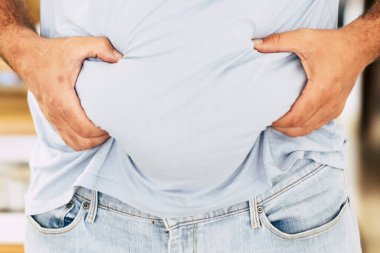 Beyaz tenli şişman adam elleriyle karnını tutuyor - diyet ve sağlıklı yaşam tarzı konsepti - abur cubur sonuçları - arka planda ve karantina koronavirüsü sonucunda