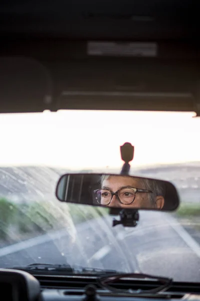 Adult senior woman driving a car looking at the road and using eyeglasses to see better - concept of drive vehicle -  insurance and travel old mature woman