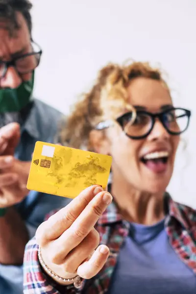 Credit card and shopping economy business concept with funny and nice adult caucasian couple with credit card - wife happy and man angry in background - focus on card