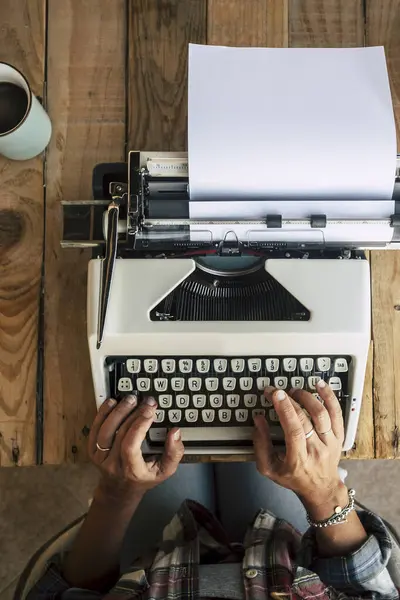 Above view of wooden desktop with alternative old vintage typewriter and woman hands working on it to write - different office and job lifestyle - vertical view of working people