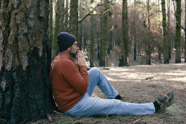 Yeşil Orman Ormanı 'nın ortasında yerde oturup rahatlayan bir adam serbest etkinliği gevşetiyor. İnsanlar ve doğa parkı hissini seviyor. Refah alternatif yaşam tarzı