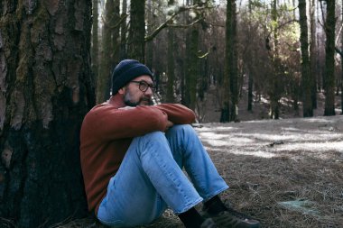  Yeşil Orman Ormanı 'nın ortasında yerde oturup rahatlayan bir adam serbest etkinliği gevşetiyor. İnsanlar ve doğa parkı hissini seviyor. Refah alternatif yaşam tarzı