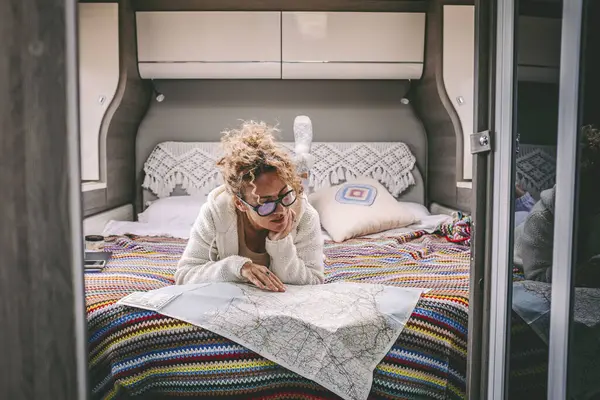 Bir sonraki yolculuk için modern bir karavanın içinde yatmayı planlayan bir kadın. İnsanlar ve Vanlife tarzı gezginler. Kapalı alan haritası için kadın görünümlü kağıt harita rehberi