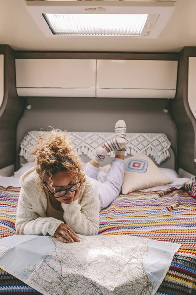 Female traveler relax inside camper van bedroom interior and looking paper road map to find next trip destination. Journey and adventure in vanlife lifestyle. woman in indoor van life leisure