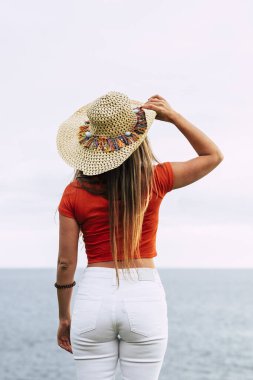 Güzel, tanınmayan genç bir kadın okyanus manzarası ve hissinin tadını çıkarıyor. Modayı takip eden insanlar ve açık hava tatil yeri kavramı.