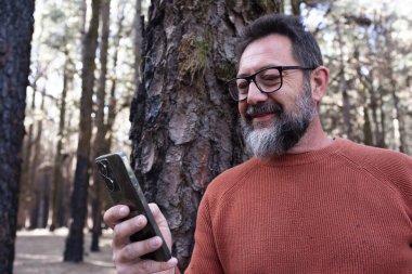 Tatilde ormanda cep telefonuyla eğlenen bir adam..