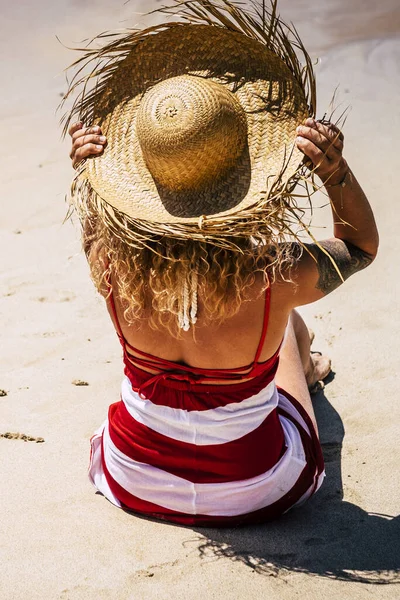 Sun and summer holiday vacation concept with people at the beach and caucasian woman viewed from back with tourist hat enjoying the day and the outdoor relax leisure activity