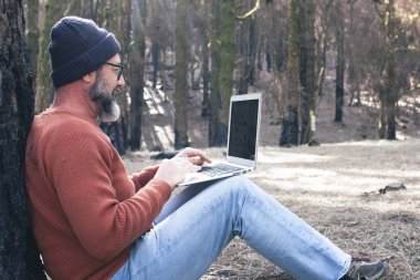  Orman odunlarında dizüstü bilgisayar kullanan bir adam teknolojinin ve boş zamanların tadını çıkarıyor. Modern insan arka planda ağaçlarla hücresel olarak konuşuyor. Seyahatte insanlar ve iletişim