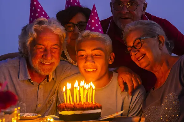 Birthday celebration at home outdoor with caucasian happy and cheerful family around a young boy teenager for his 18 years old - night colors time and blowing candles on a cake to wish a desire