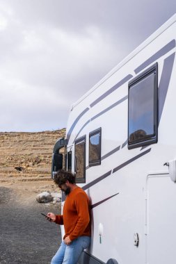 Gezgin adam modern bir karavanın önünde telefon uygulaması kullanarak yolculuk planı yapıyor ve bir sonraki durak ise akıllı telefon uygulaması. Manzaralı bir yer ve seyahat tarzı. Araç kiralama