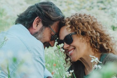 İlişki yaşam tarzında aşk ve romantizm. Çiftler randevudan ve hayattan keyif alıyorlar. Yeşil doğa tarlasında beyaz çiçeklerle oturuyorlar. Mutlu erkek ve kadın açık havada eğleniyor