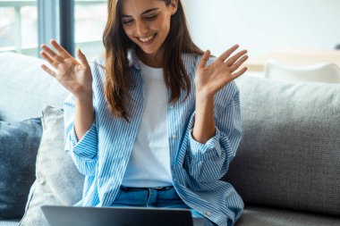 Laptop ekranına bakan, el sallayan, evden arkadaşlarıyla görüntülü konuşma yapan mutlu genç ve çekici bir kadın. Gülümseyen milenyum öğretmeni merhaba diyor. Merhaba jest yapıyor, müşterileri selamlıyor..