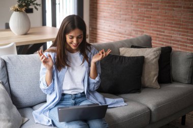 Genç bir kadın bilgisayarla uzaktan arkadaşlarını arıyor. Video konferans bağlantısı. Ev içi eğlence aktivitesi. Kanepede oturan bilgisayarlı kadın.. 