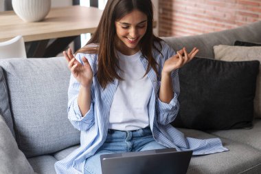Genç bir kadın bilgisayarla uzaktan arkadaşlarını arıyor. Video konferans bağlantısı. Ev içi eğlence aktivitesi. Kanepede oturan bilgisayarlı kadın.. 