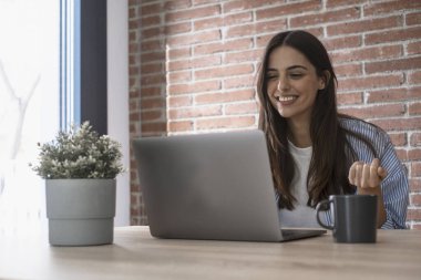 Arkadaşlarını ya da iş adamlarını çağırmak için dizüstü bilgisayar kullanan mutlu genç bir bayan ekranda gülümseyip el sallıyor.. 